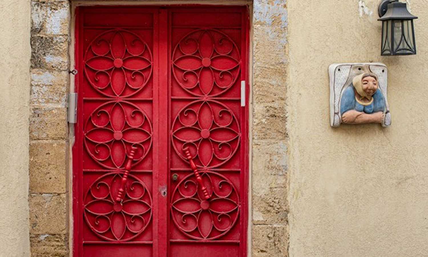 Decorative red double doors framed by weathered stone on a historic building in Neve Tzedek, Tel Aviv.